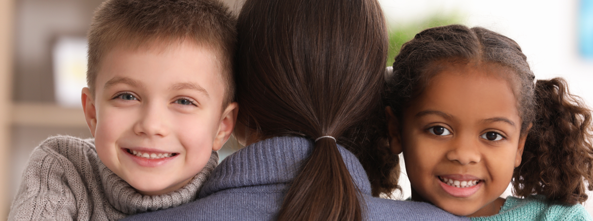 Twi adoptive children of different ethnicity hugging their adoptive mother.