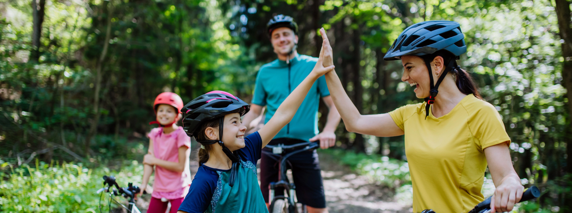 A young family with little children preapring for bike ride, standing with bicycles in nature and high fiving.