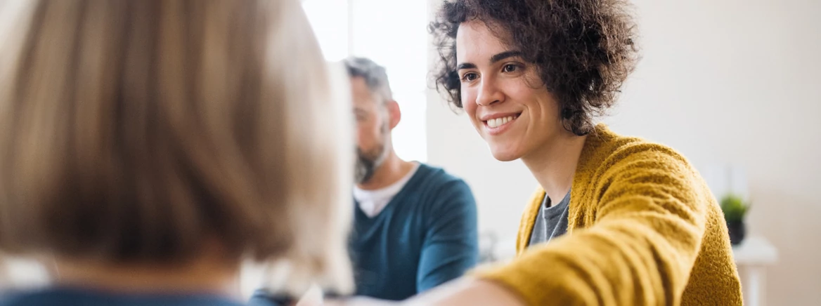 Serious men and women sitting in a circle during group therapy, supporting each other.