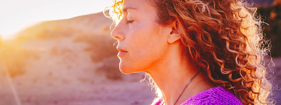 Close up sunset portrait of attractive woman with closed eyes and sun in back light. Dreaming and enjoying feeling concept lifestyle emotion. Serene female people outdoor with curly hair