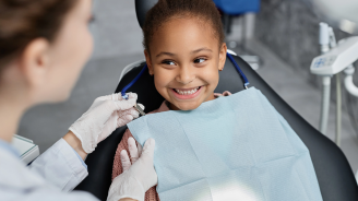 A female child in a dental child while a female dentist conducts a dentist appointment.