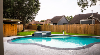 A large free form gray grey accent swimming pool with turquoise blue swim water in a fenced in backyard in a suburb neighborhood.