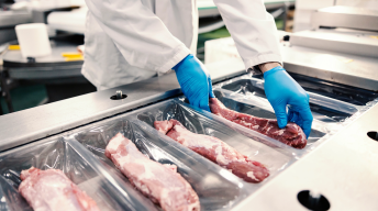 Close up of a food factory worker packing meat into the plastic on a packing machine. Expense of a meat.