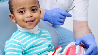 baby boy in a dentist&#039;s chair holding a toothbrush in his hand and smiling at the camera. Dental Care