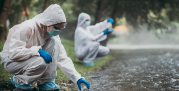 Two scientists in protective suits taking water samples from the river.
