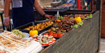Festival of street food. A wooden counter with a variety of dishes sold outdoors in the local market. Toasted pita bread, vegetables and meat