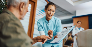 Young nurse assisting senior man in filling paperwork at doctor&#039;s office.