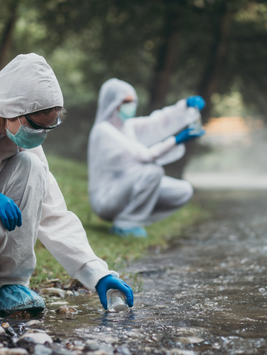 Two scientists in protective suits taking water samples from the river.