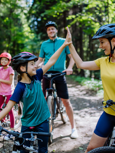 A young family with little children preapring for bike ride, standing with bicycles in nature and high fiving.