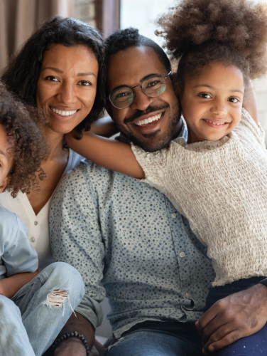 Portrait of happy african ethnicity family bonding with small kids on comfortable sofa. Cheerful loving devoted mixed race couple cuddling cute little children siblings, relaxing at weekend at home.