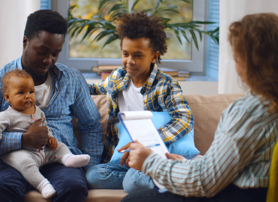 Social worker consulting smiling young single father with kids at home. Case worker woman visiting african man with schoolboy son and baby daughter providing consultation