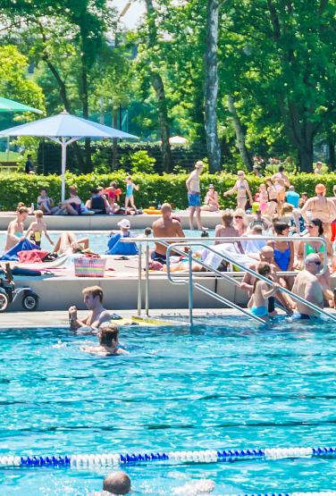 A public swimming pool with people swimming and enjying the weather on a sunny summer day